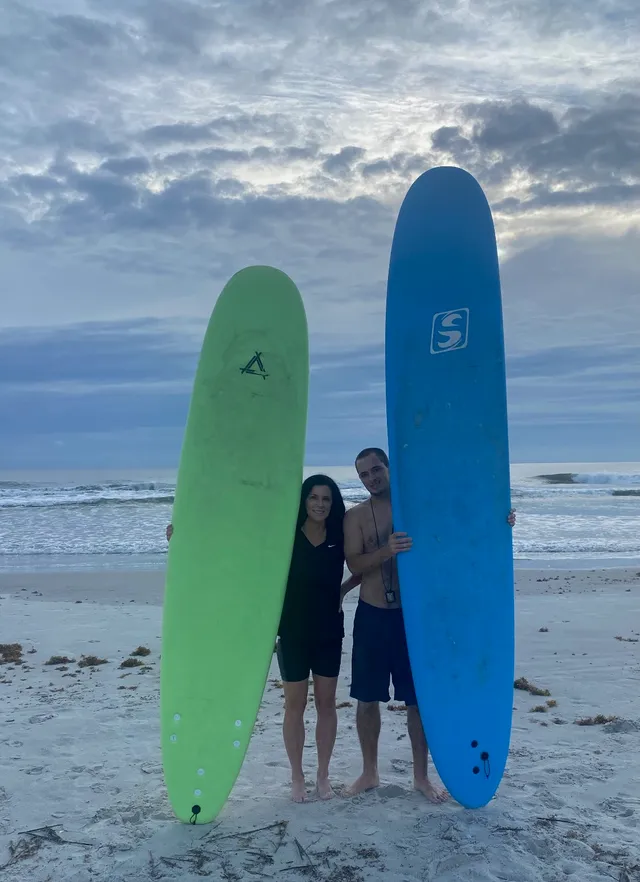 Two surf students posing on the beach with their soft-top surfboards after a lesson