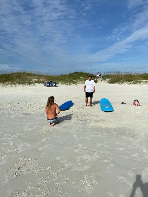 Instructor talking with a student on the sand next to their surfboards before paddling out