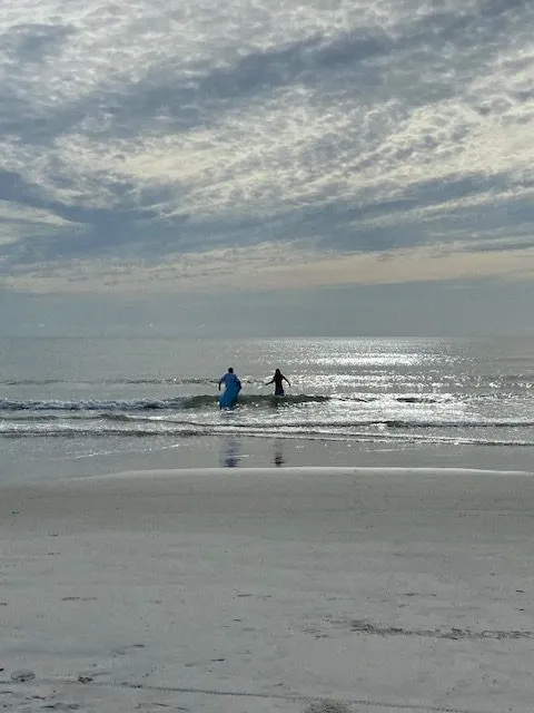 Two surfers wading out through the shorebreak at sunset